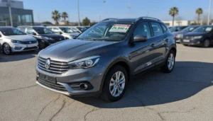 SUV 7 places gris garé sur un parking de concessionnaire, vue de trois quarts avant, étiquette prix sur pare-brise, lumière naturelle